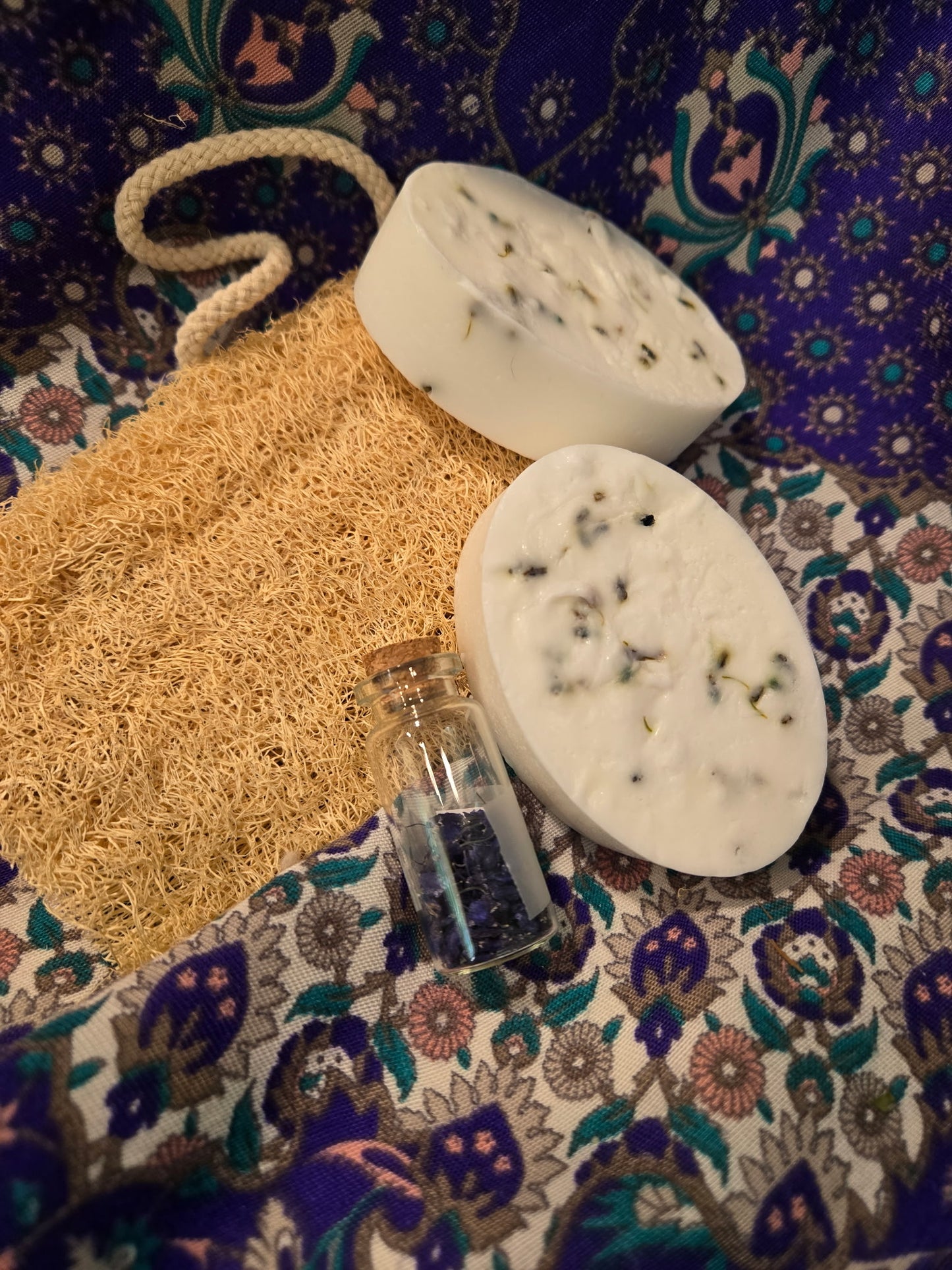 Two soap bars with a loofah and a small bottle on a patterned fabric background