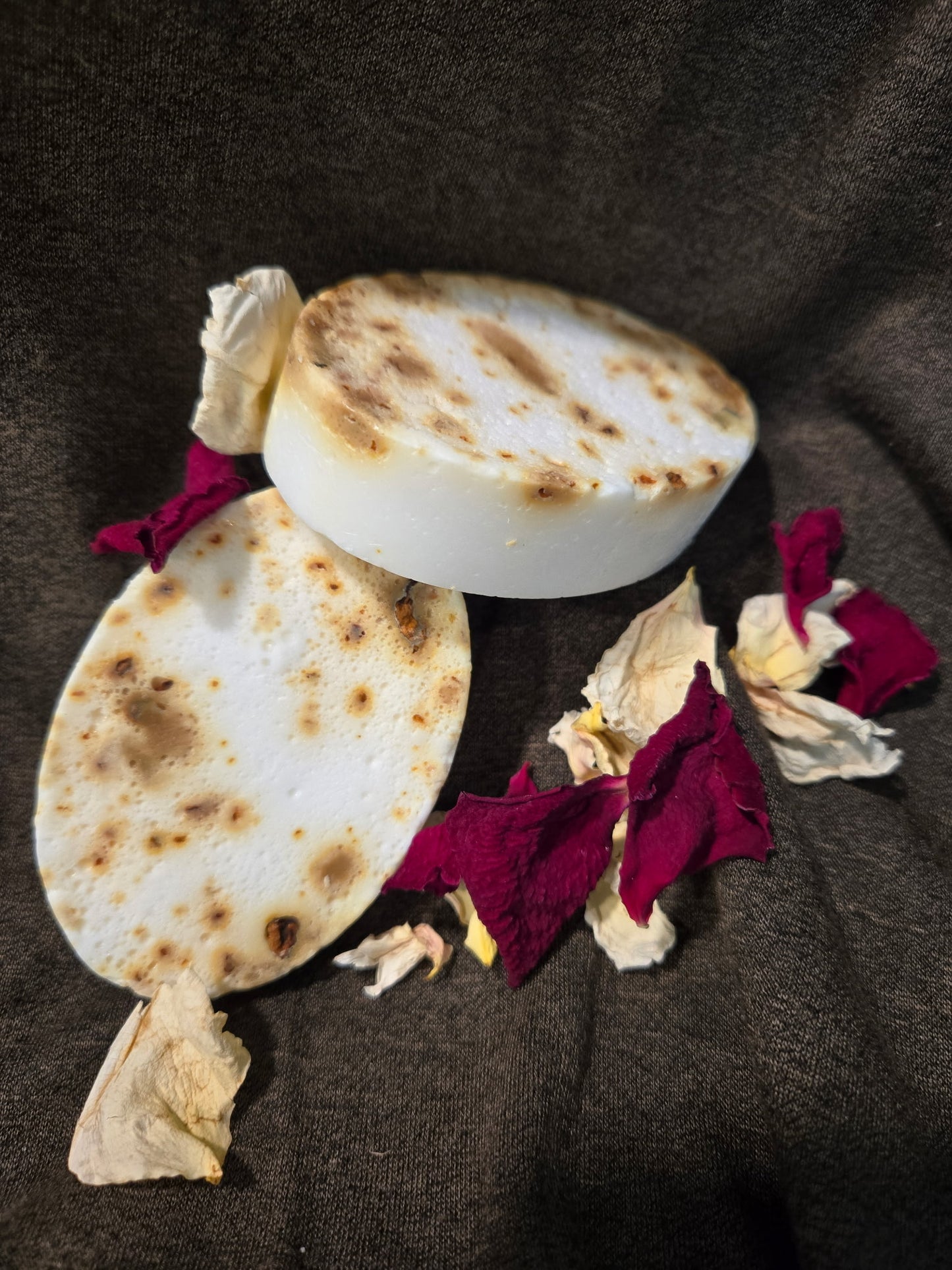 Two oval soaps with flower petals on a dark fabric background