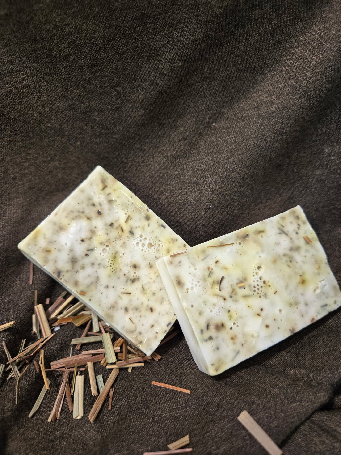 Two soap bars with natural ingredients on a brown fabric background