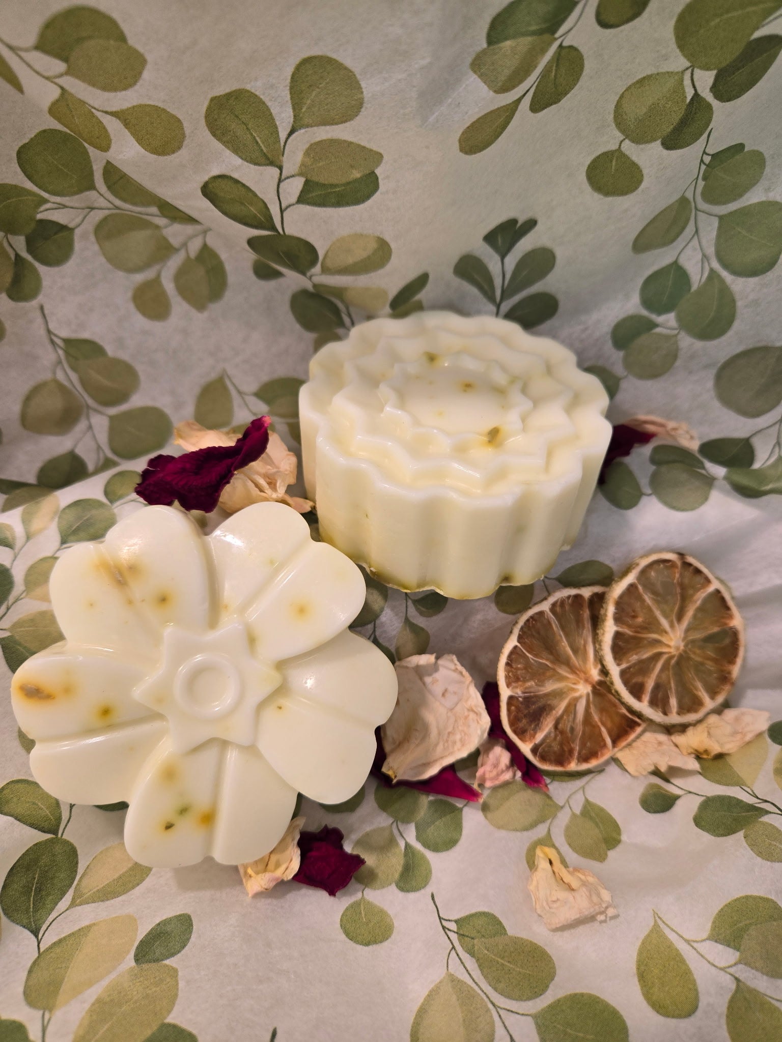 Two white soaps with floral designs on a decorative surface with leaves and flowers.
