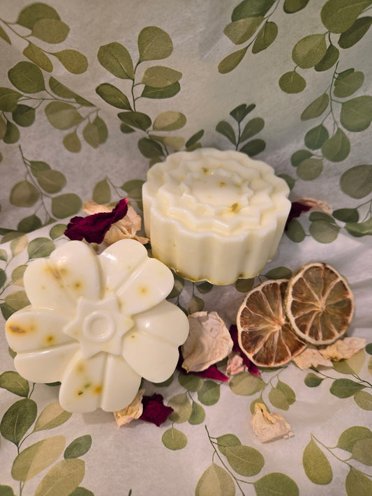 Two white soaps with floral designs on a decorative surface with leaves and flowers.