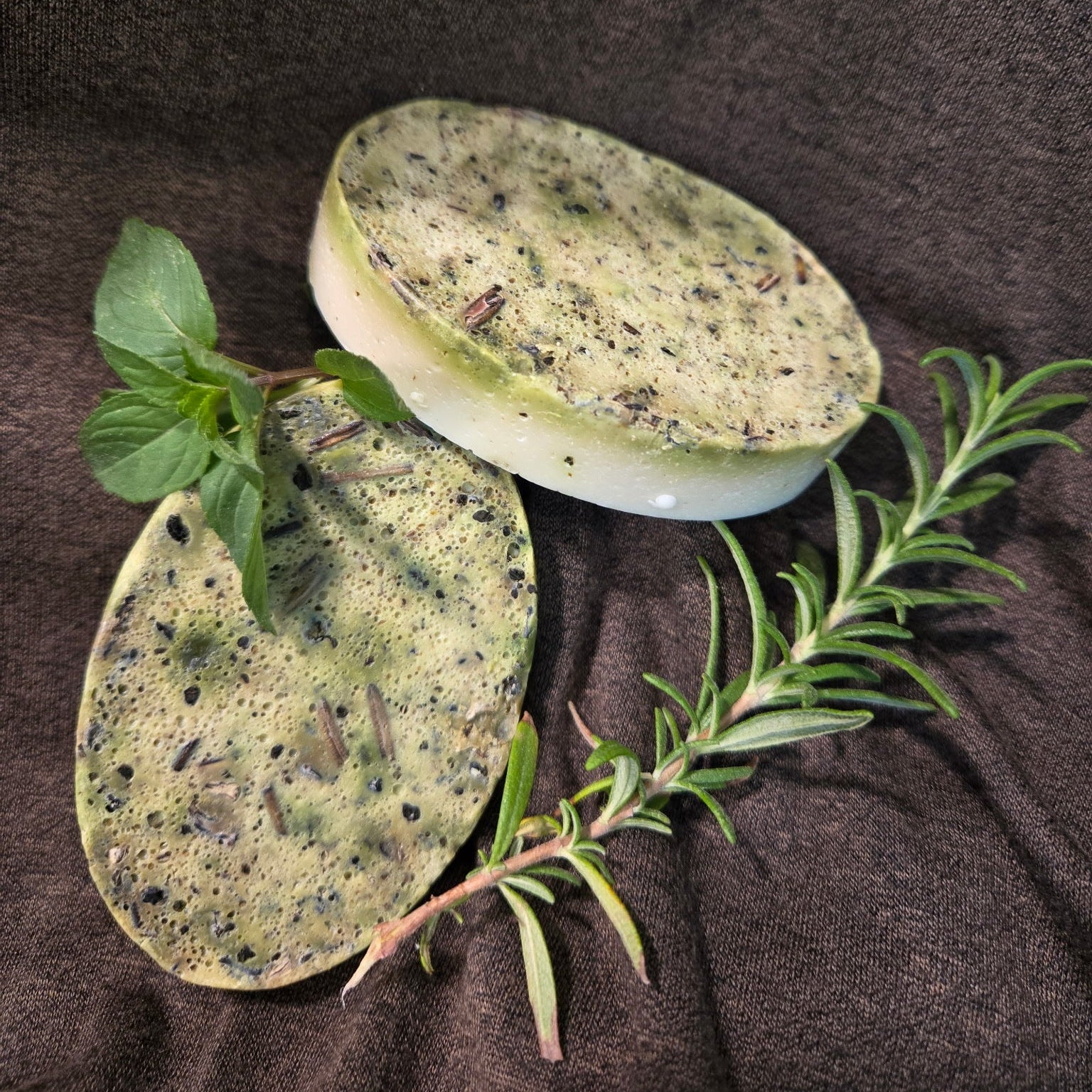Two green soaps with herbs on a brown fabric background